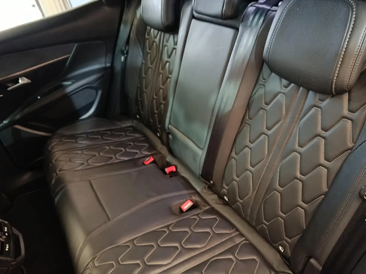 Vue intérieure côté arrière droit montrant la banquette en cuir noir avec surpiqûres hexagonales du Peugeot 3008 Hybrid 225 GT Pack.