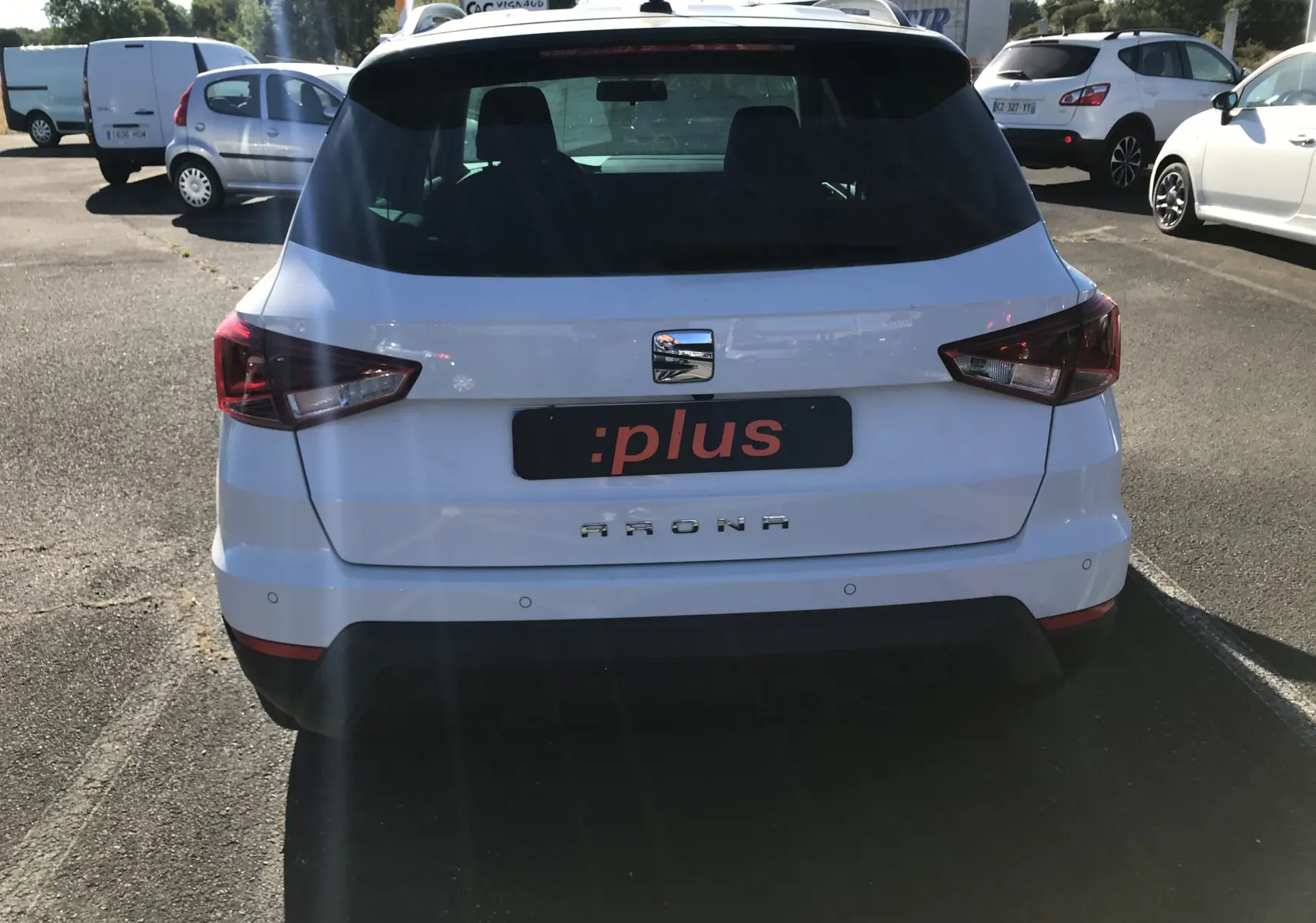 Vue arrière d'un SEAT Arona blanc avec toit noir, affichant ses feux arrière anguleux et son logo central chromé.