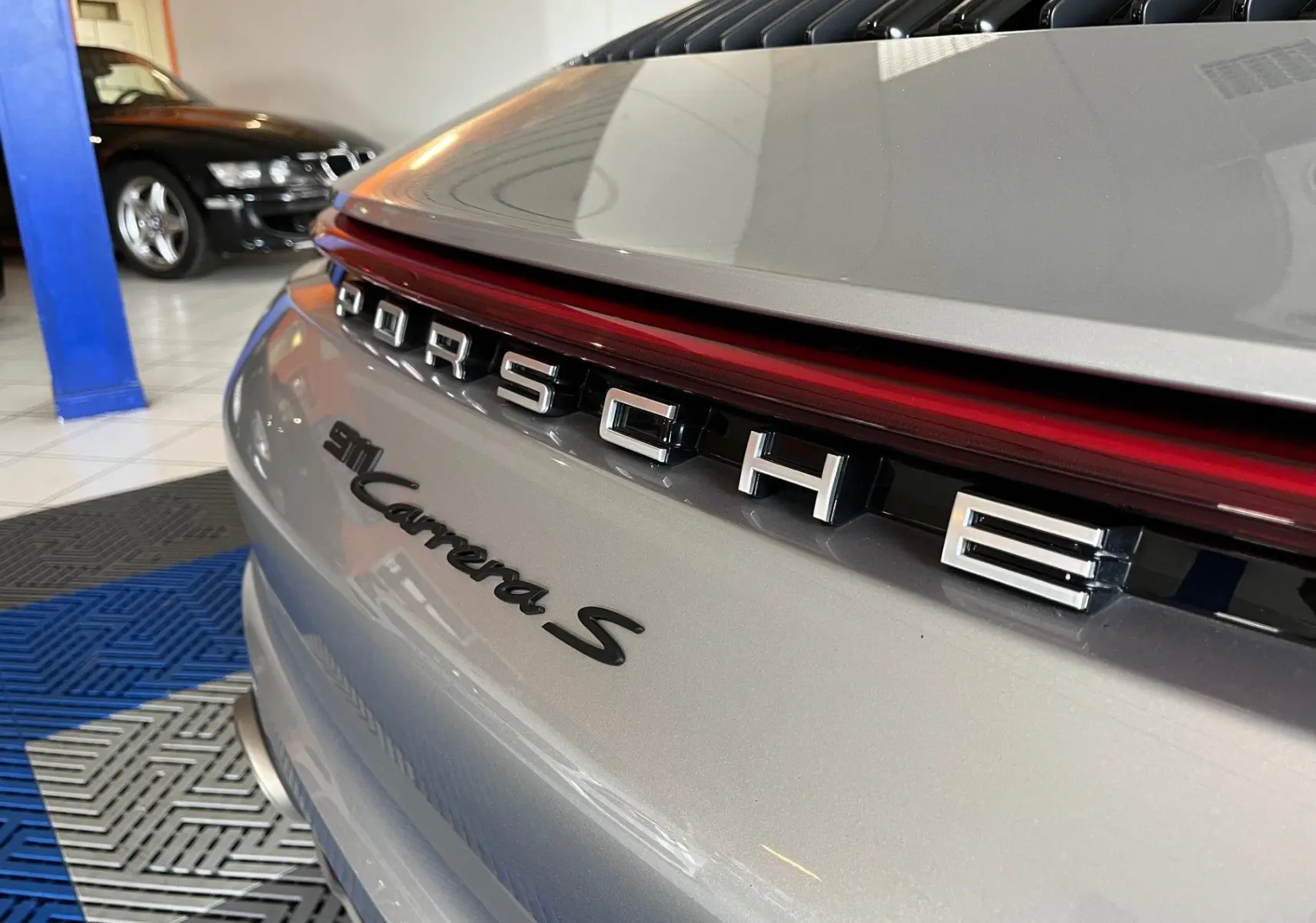 Gros plan arrière droit sur la Porsche 911 Carrera S argent GT, mettant en valeur le logo et la bande lumineuse rouge.