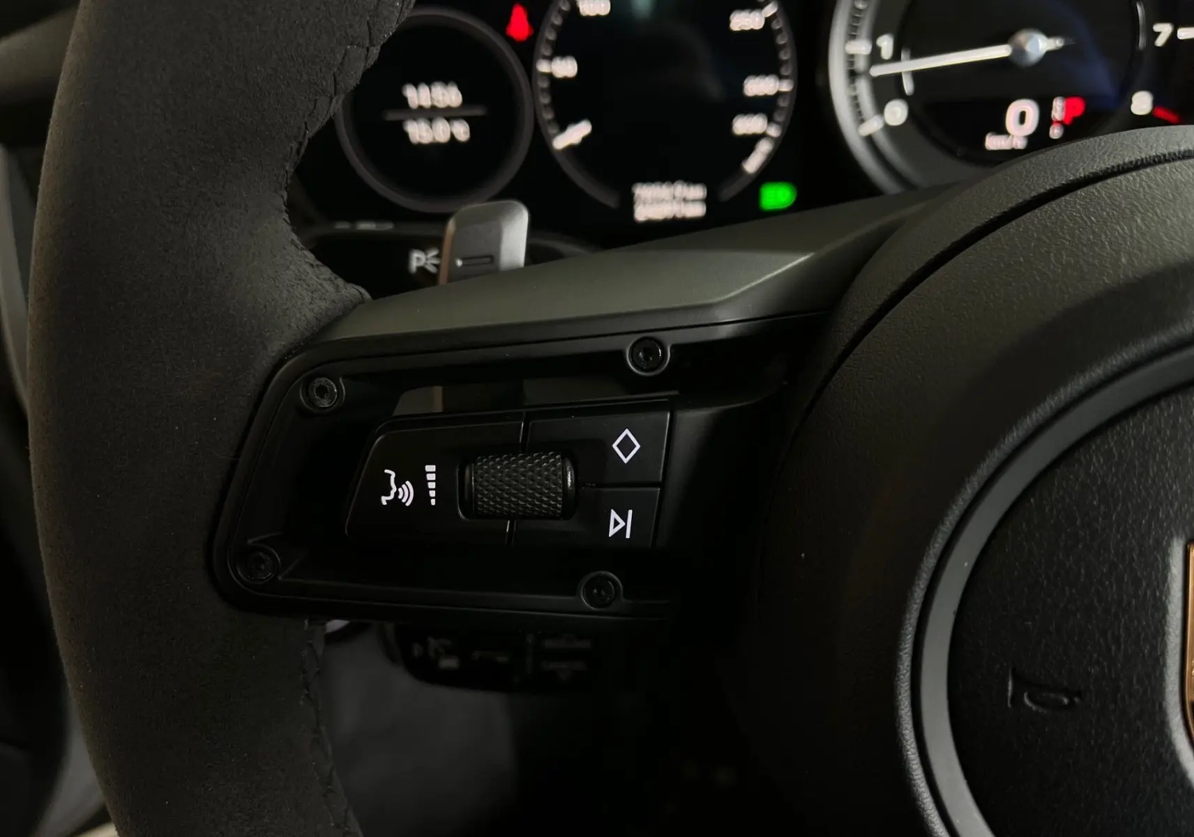 Gros plan sur les commandes gauche du volant en Alcantara noir de la Porsche 911 Carrera S 2019, avec tableau de bord digital en arrière-plan.