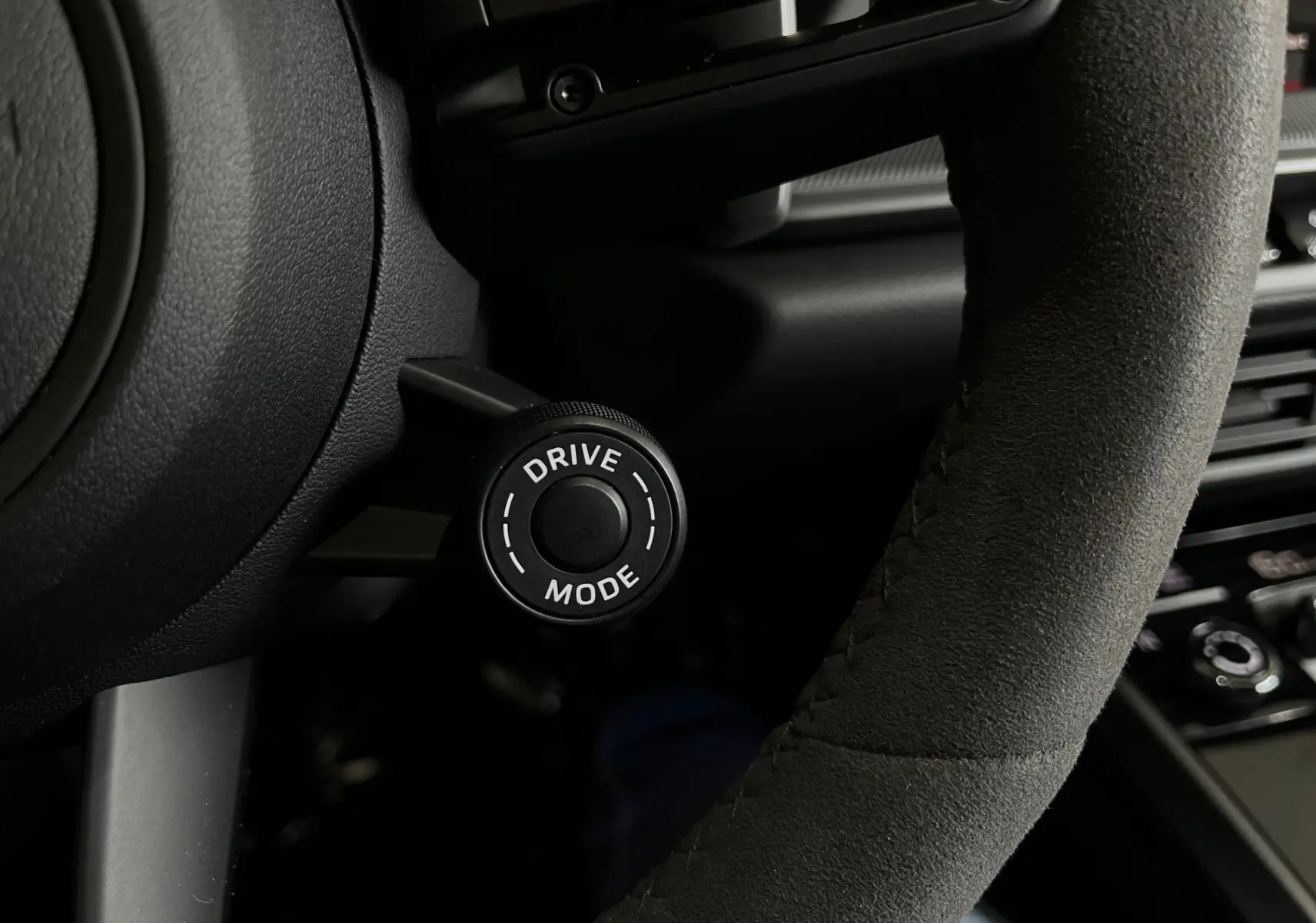 Gros plan sur le bouton Drive Mode à gauche du volant en Alcantara noir dans l'habitacle d'une Porsche 911 Carrera S 2019.