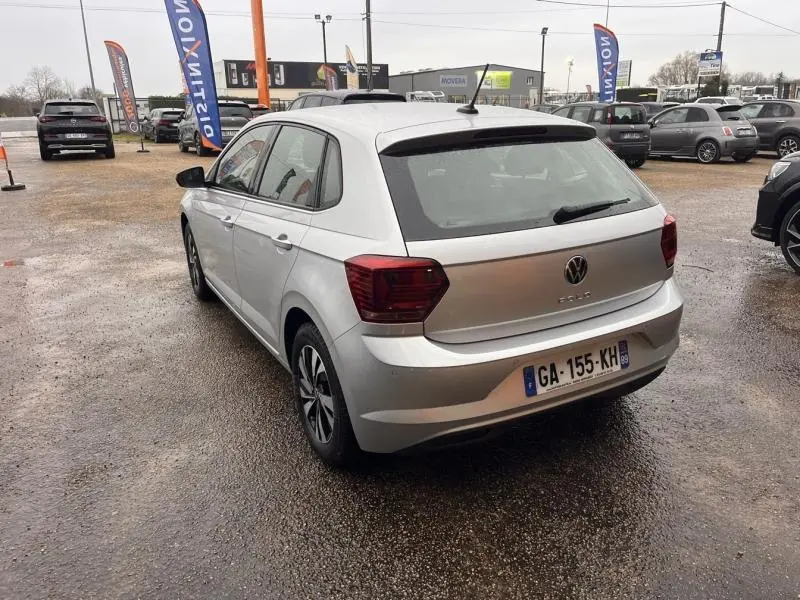 Vue 3/4 arrière droite d'une Volkswagen Polo gris Urano avec jantes alu, sur un parking extérieur humide.