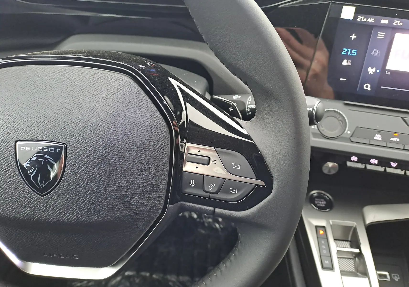 Vue rapprochée du volant noir de la Peugeot 308 2025 avec commandes intégrées et tableau de bord digital en arrière-plan.