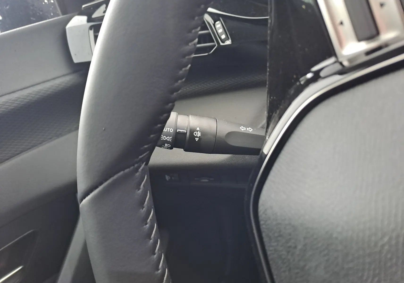Gros plan sur le volant en cuir noir et la commande des feux à gauche dans l'habitacle d'une Peugeot 308 blanche.
