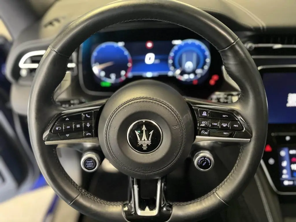 Gros plan sur le volant cuir multifonction de la Maserati Grecale bleu, avec commandes de régulateur et bouton Drive Mode visible.