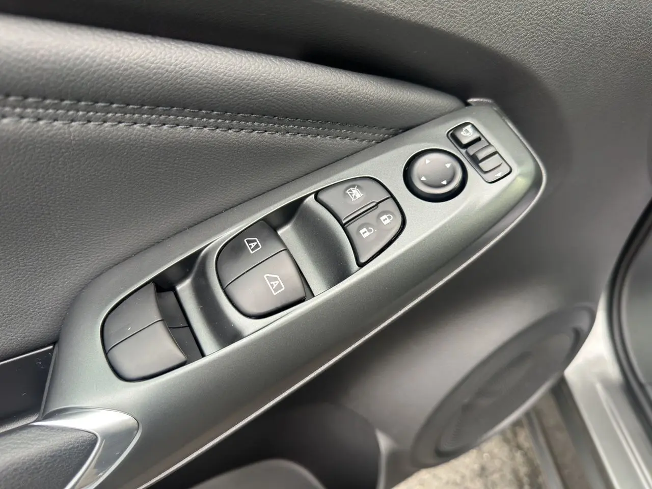 Gros plan sur les commandes de lève-vitres et rétroviseurs sur la porte côté conducteur du Nissan Juke gris squale.