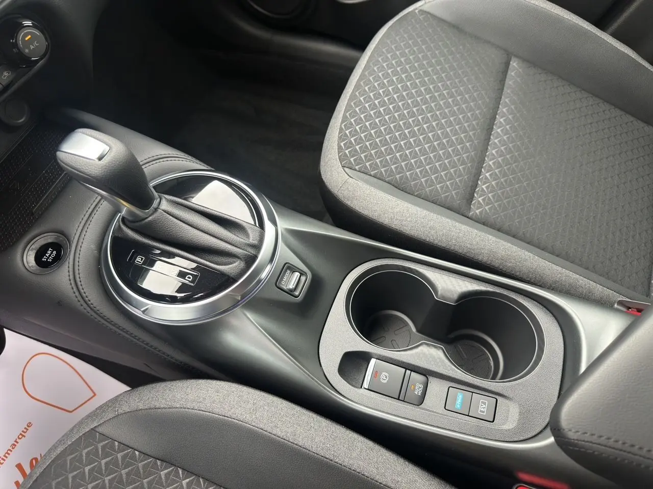 Gros plan sur la console centrale du Nissan Juke gris, avec levier de vitesse automatique et sièges en tissu noir.