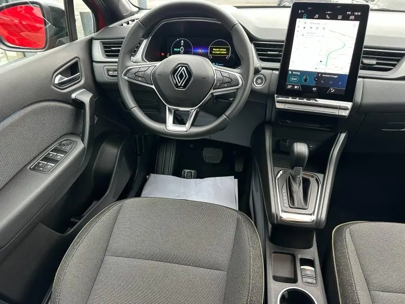 Vue intérieure avant du Renault Captur 2025, volant au centre, écran tactile vertical et rétroviseur rouge visible.