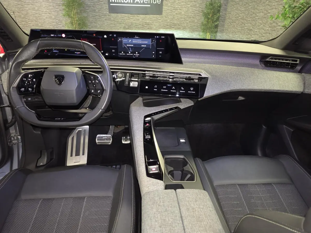 Vue intérieure avant du Peugeot 3008 gris 2025, tableau de bord avec écran panoramique et volant compact cuir noir.