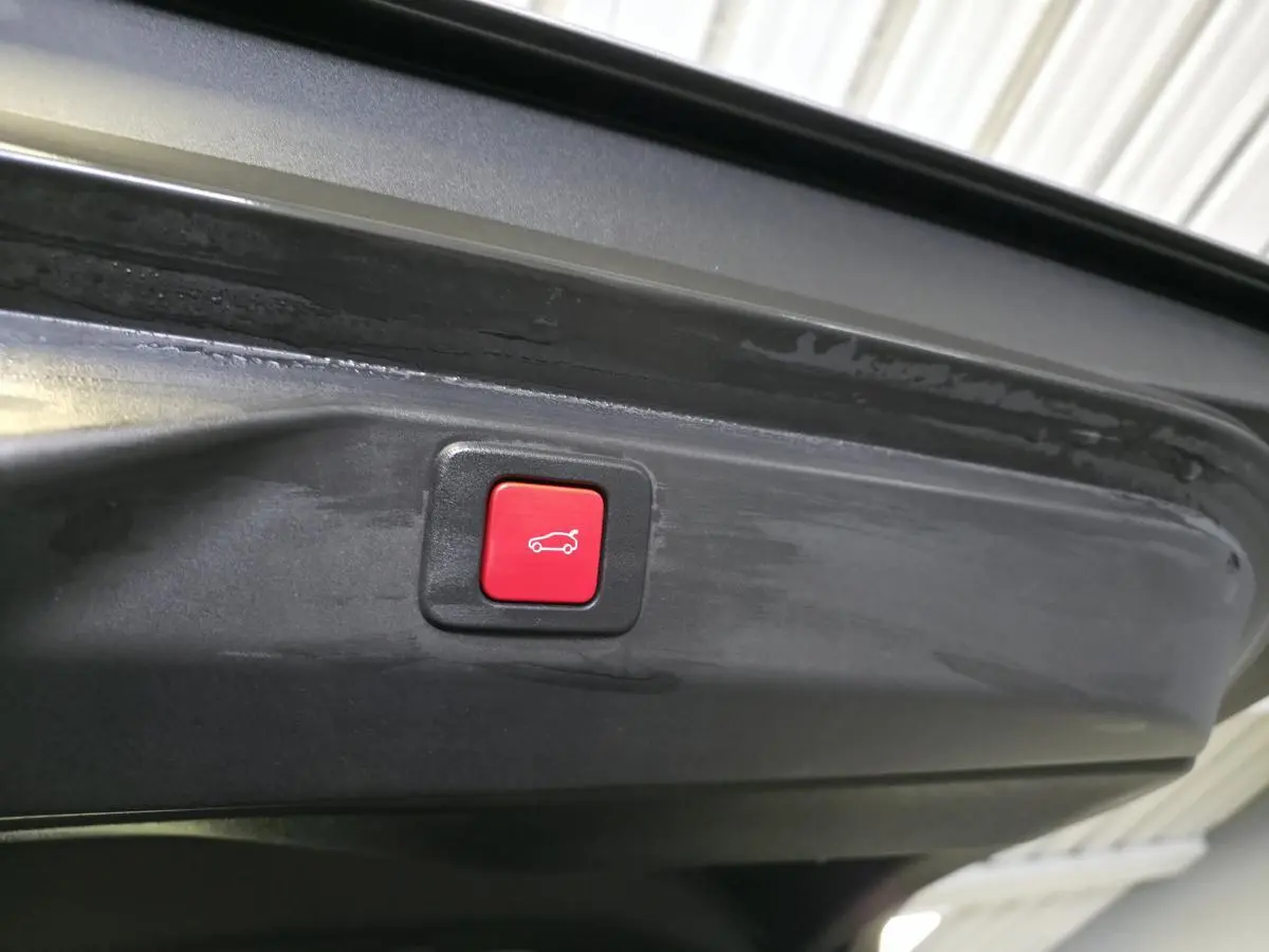 Bouton rouge de fermeture électrique du hayon visible sur l'intérieur du coffre d'un Peugeot 3008 gris.