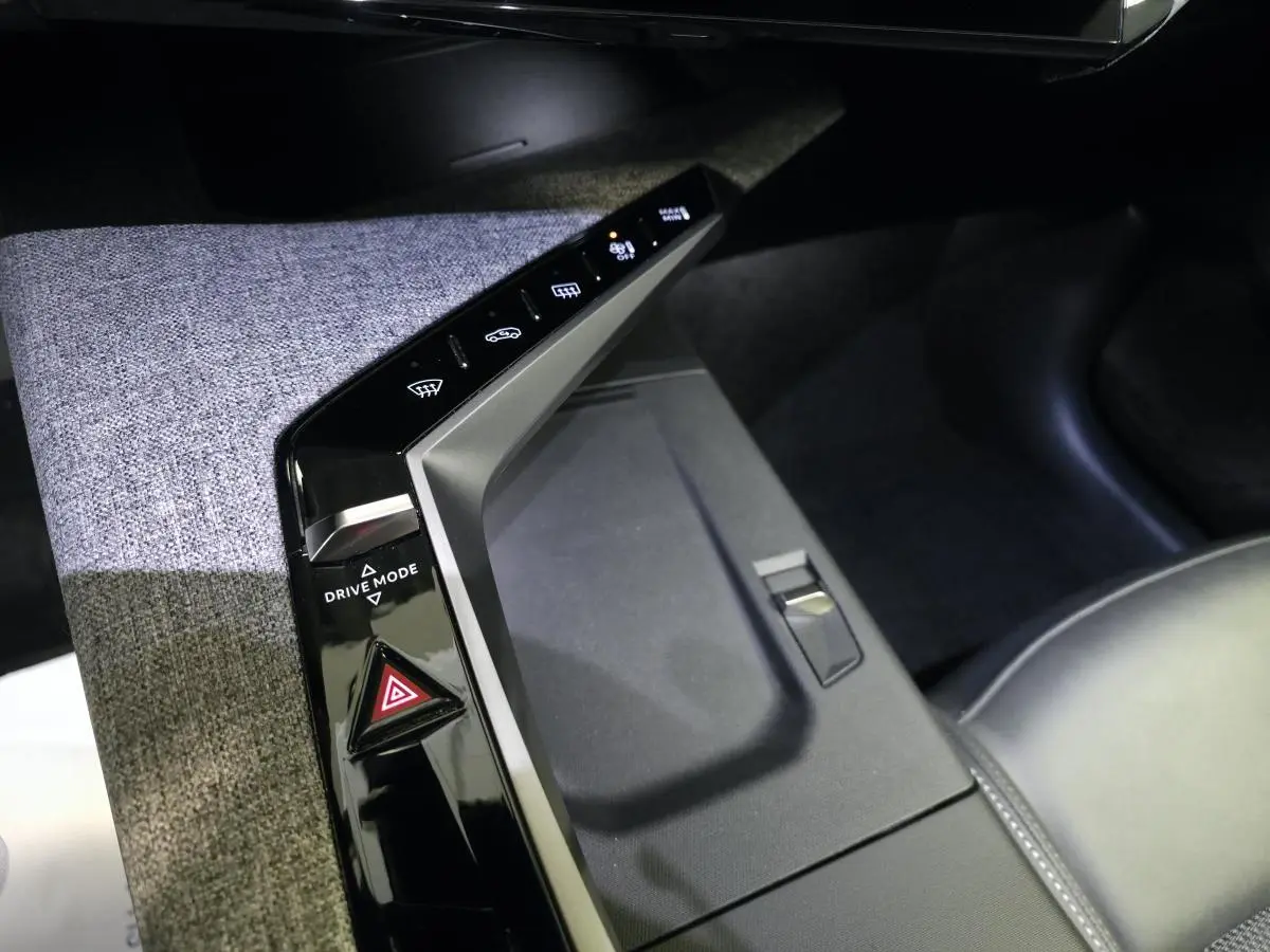 Vue rapprochée de la console centrale tissu gris et noir laqué du Peugeot 3008 Hybrid 2025 avec commandes tactiles et bouton Drive Mode.
