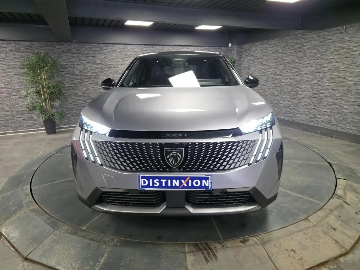 Vue frontale d'un Peugeot 3008 gris métallisé 2025 avec calandre noire à motif géométrique et feux LED griffés allumés.
