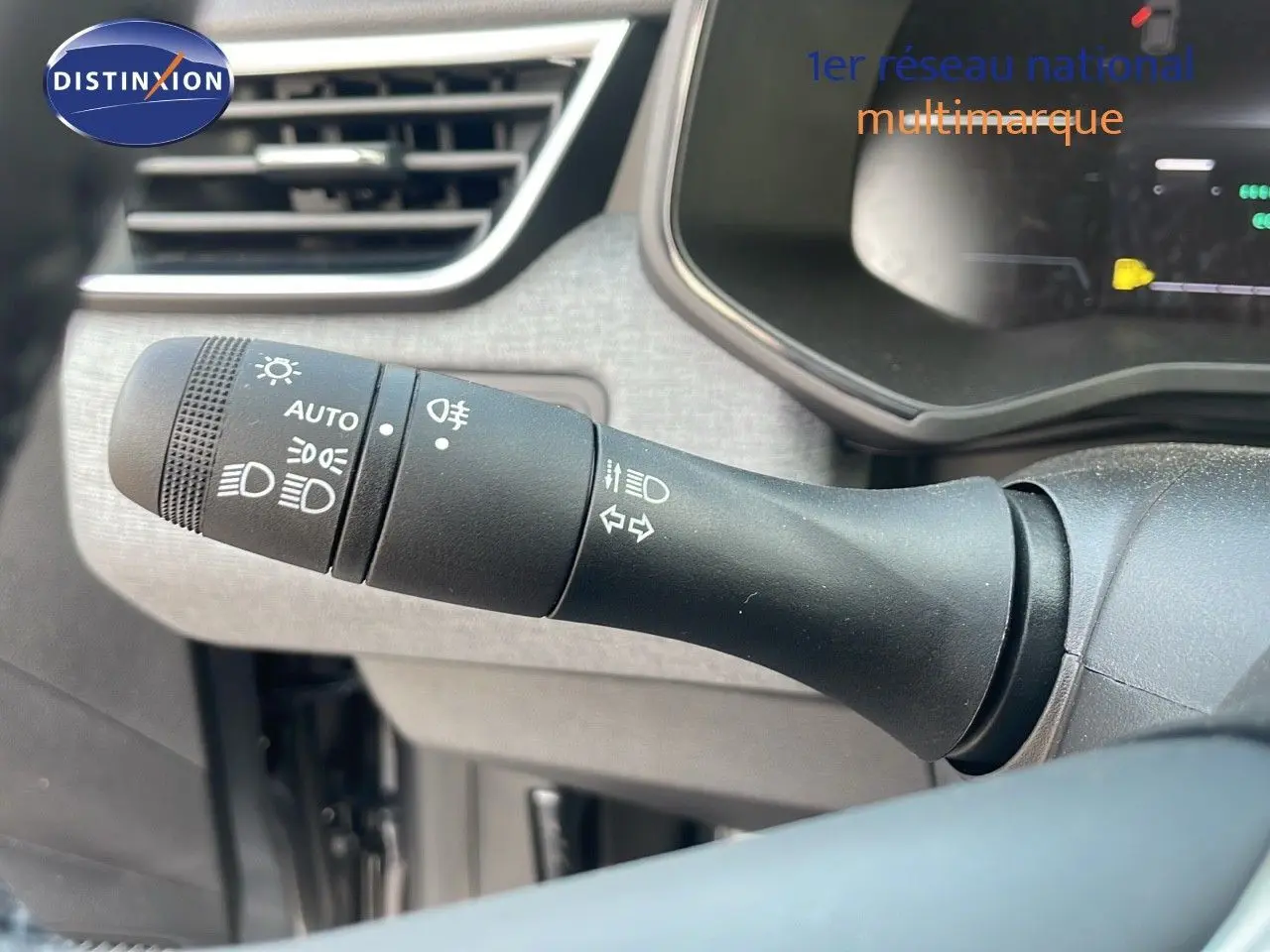 Gros plan sur la commande des feux d’un Renault Clio gris schiste, intérieur tissu gris-noir visible en arrière-plan.
