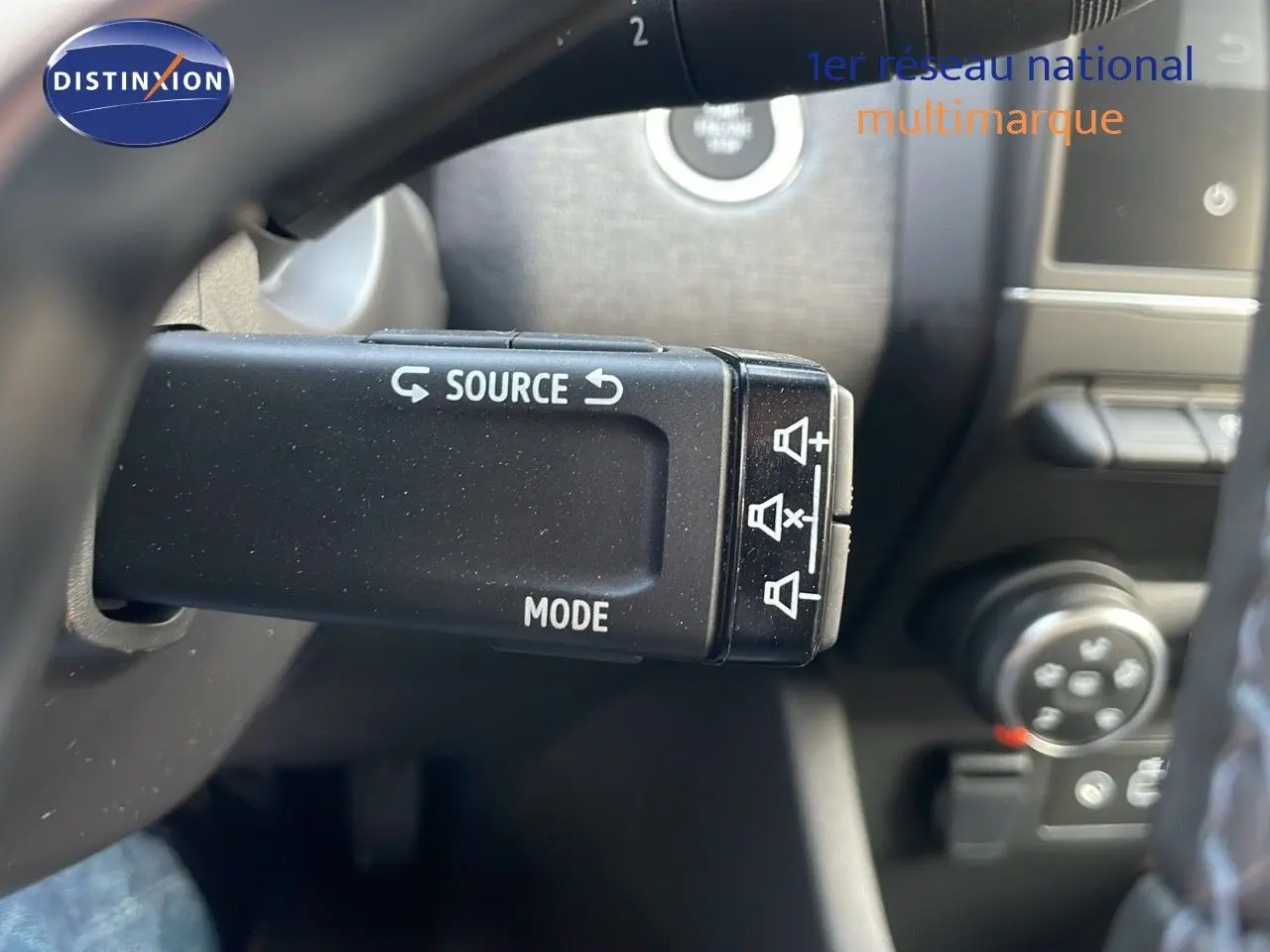 Gros plan sur la commande au volant de la Renault Clio 2025, avec boutons source et mode visibles en intérieur gris noir.