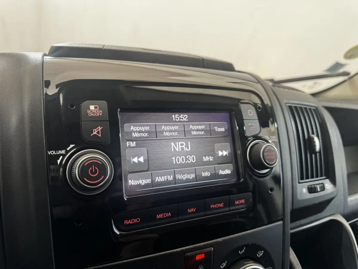 Gros plan sur l’écran tactile multimédia noir du tableau de bord du Citroën Jumper blanc, affichant une radio FM NRJ.