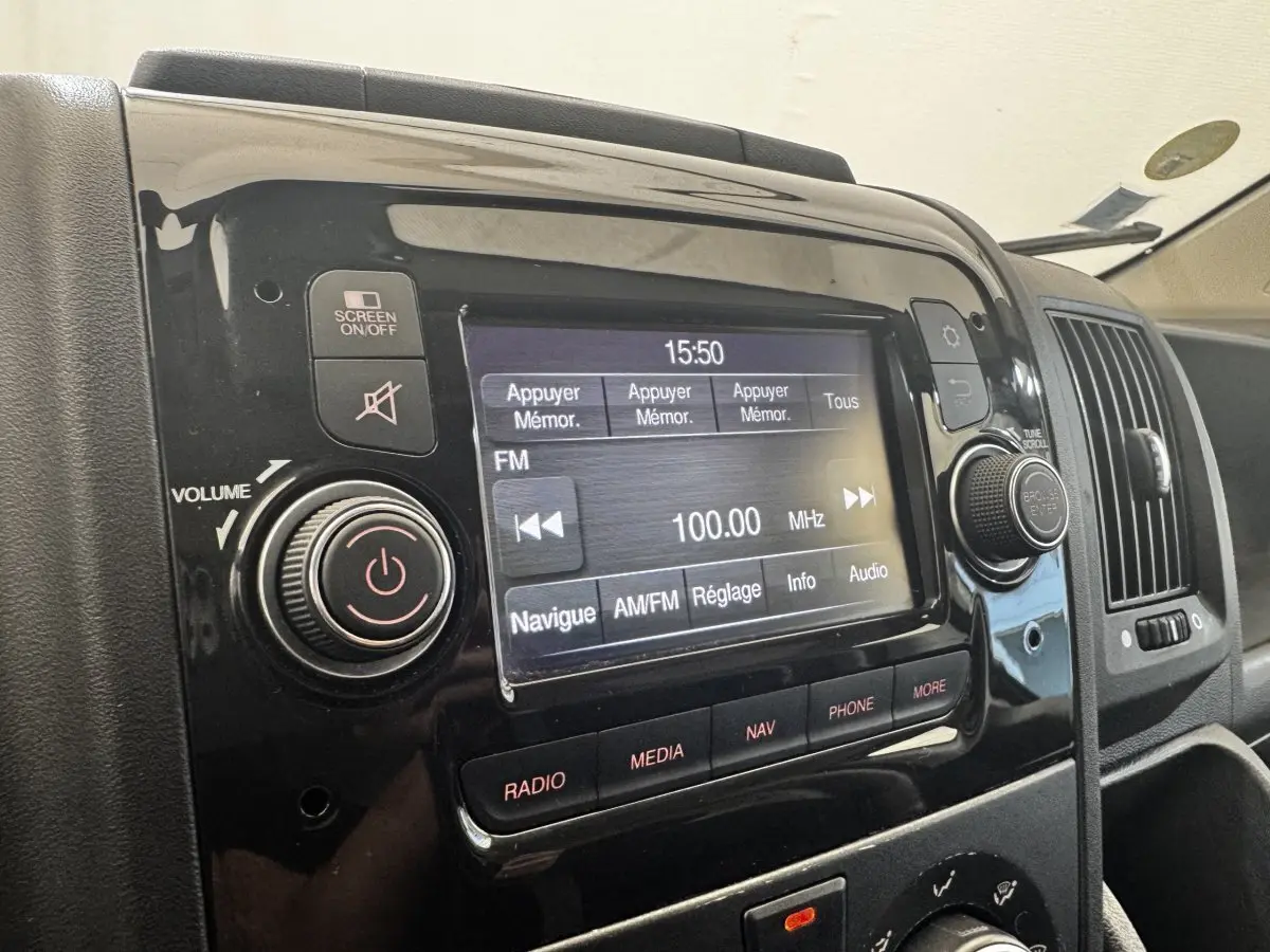 Gros plan sur l’écran tactile multimédia noir du tableau de bord du Citroën Jumper blanc, affichant la radio FM à 100 MHz.