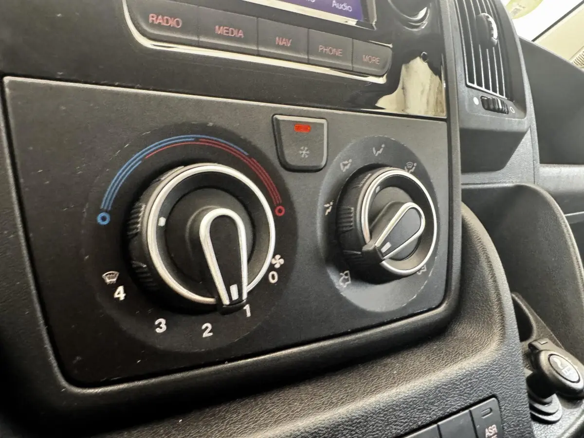 Gros plan sur les commandes de climatisation et la console centrale du Citroën Jumper blanc, intérieur avant.