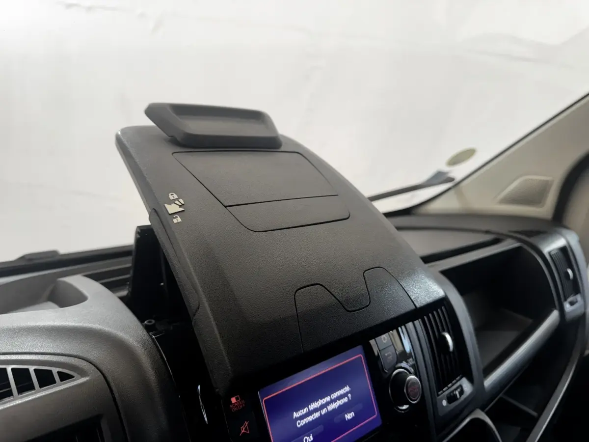 Vue intérieure rapprochée du tableau de bord noir du Citroën Jumper 2023 avec écran tactile et rangement ouvert.