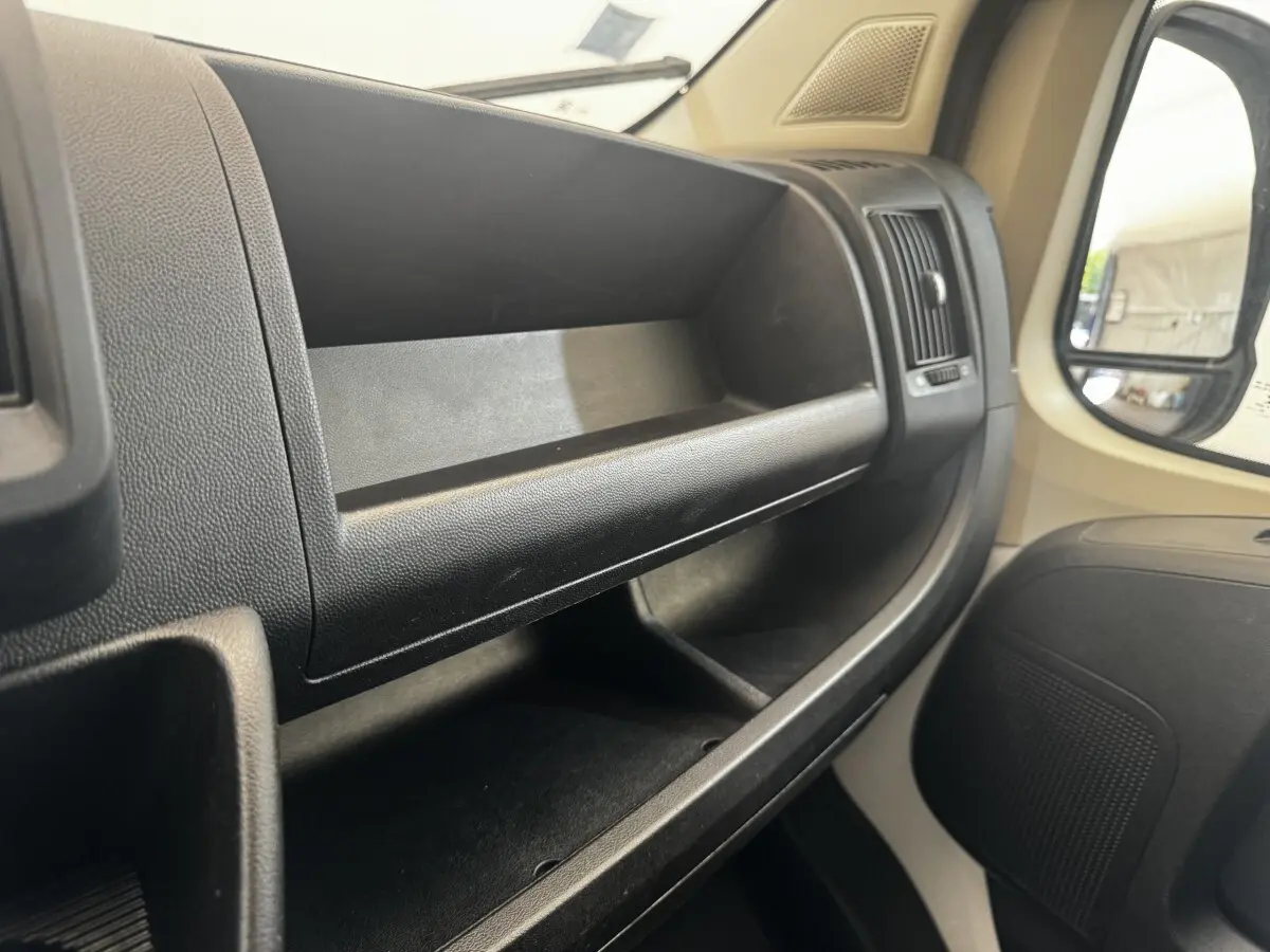 Vue intérieure côté passager du tableau de bord noir avec rangements ouverts et partie de la portière beige du Citroën Jumper 2023.