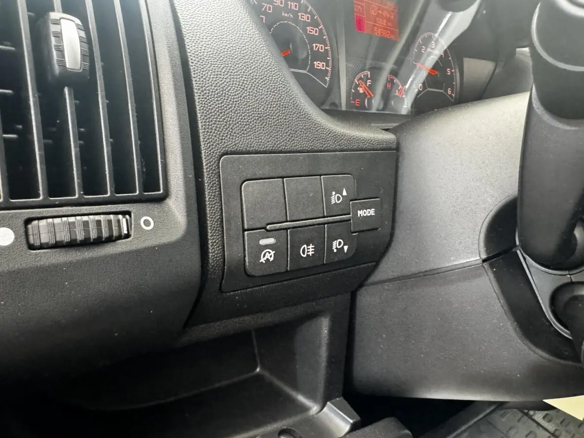 Gros plan sur les commandes d’éclairage et tableau de bord noir du Citroën Jumper 33 L1H1 blanc, vue intérieure côté conducteur.