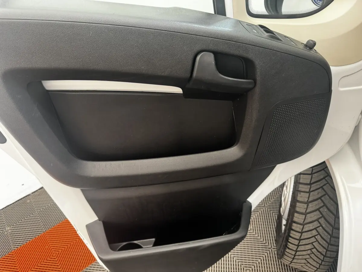 Vue rapprochée de la porte avant gauche blanche du Citroën Jumper 2023 avec poignée noire et rangement intégré.