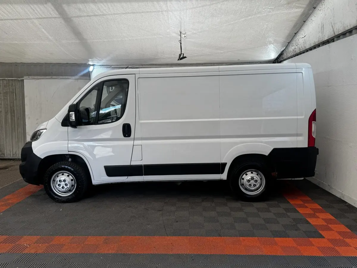 Vue de profil côté gauche d’un fourgon blanc Citroën Jumper 33 L1H1 avec jantes acier et protections noires.