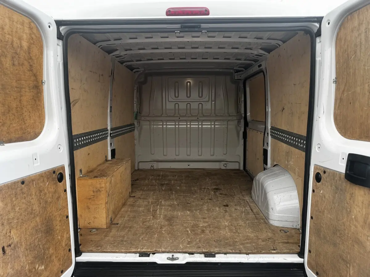 Vue arrière intérieure du Citroën Jumper blanc 33 L1H1 avec cloison pleine et revêtement bois du coffre.