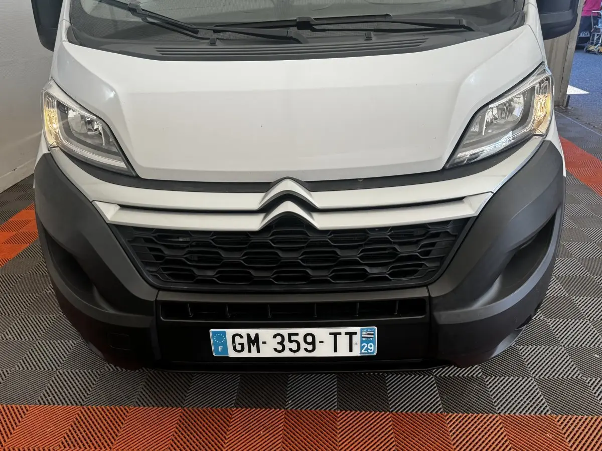 Vue frontale rapprochée du Citroën Jumper blanc avec calandre noire et phares allumés sur sol à damier noir et orange.