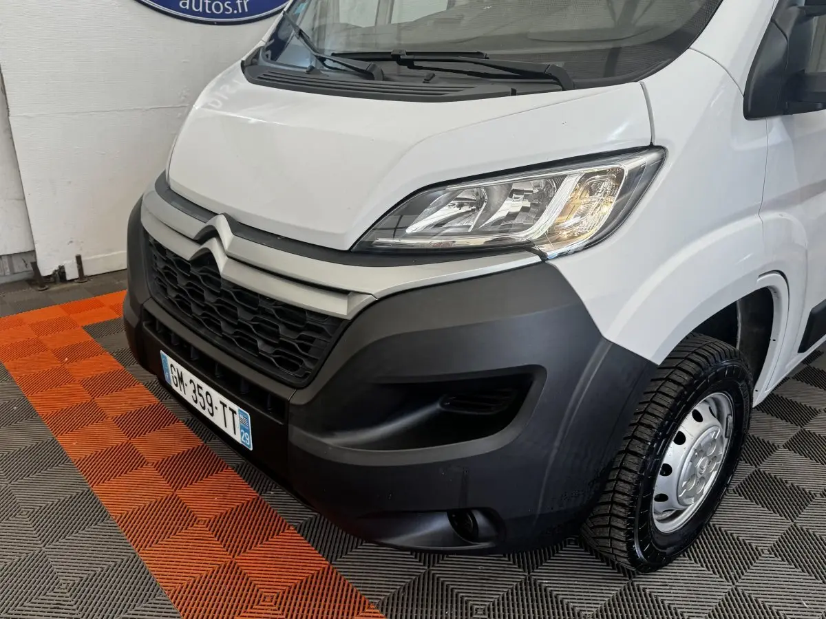 Vue 3/4 avant droit d’un Citroën Jumper blanc avec pare-chocs noir et jante acier sur sol damier orange et gris.