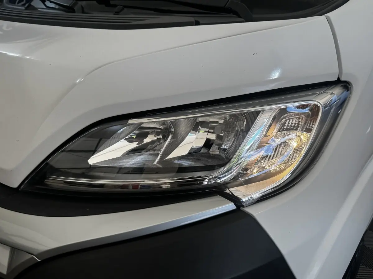 Gros plan sur le phare avant droit du Citroën Jumper blanc 2023, mettant en valeur son design moderne et ses détails chromés.
