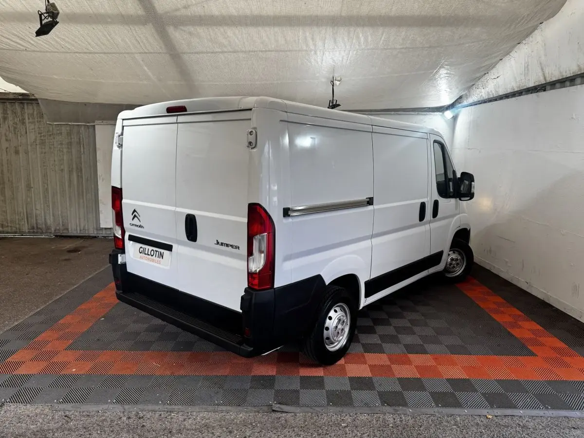 Vue 3/4 arrière droite d’un utilitaire Citroën Jumper blanc stationné en intérieur sur sol à damiers gris et orange.