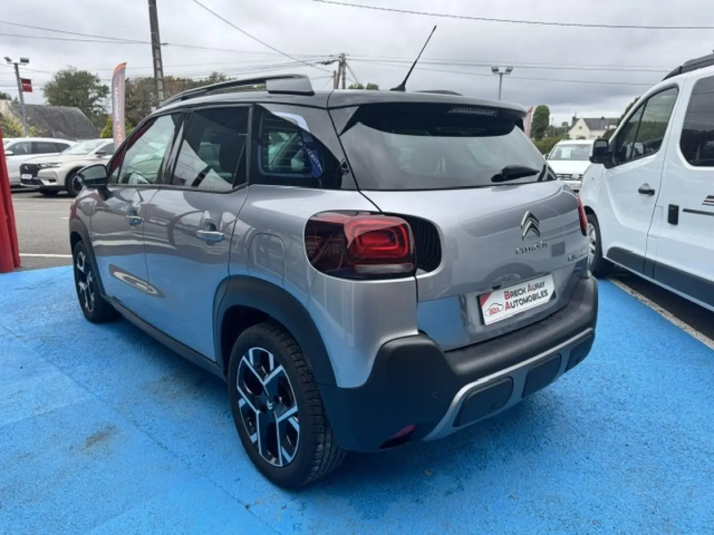 Vue 3/4 arrière droite d'un Citroën C3 Aircross gris acier avec barres de toit et jantes alu noires.