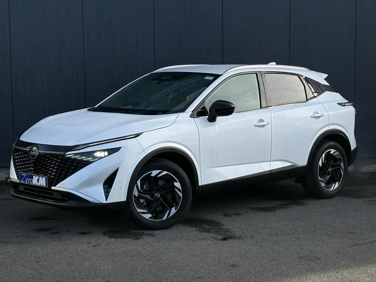 Nissan Qashqai blanc nacré en 3/4 avant droit, avec jantes alliage noires et toit contrasté noir.