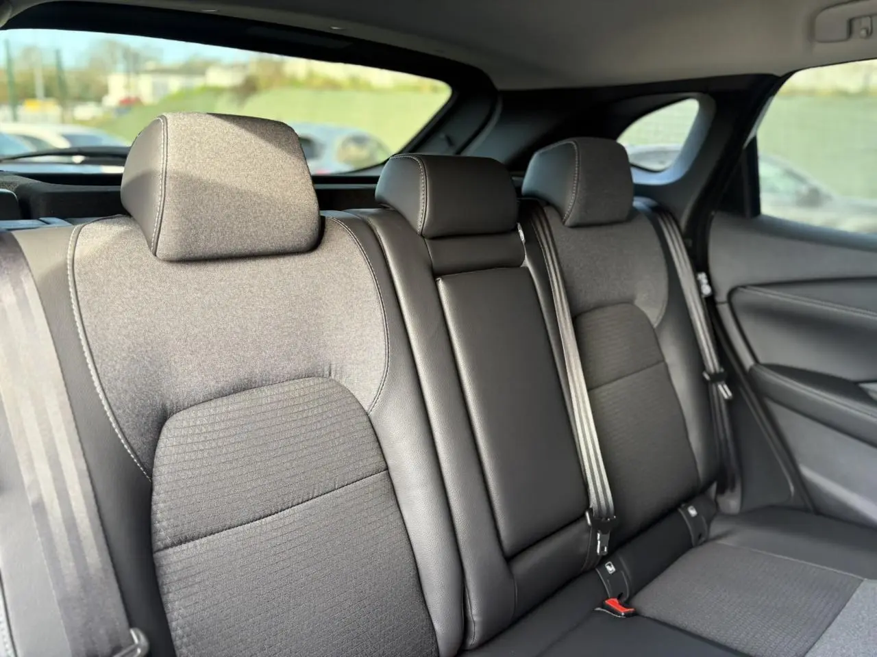 Vue intérieure des sièges arrière gris foncé du Nissan Qashqai III blanc nacré, avec appuie-têtes et ceintures visibles.