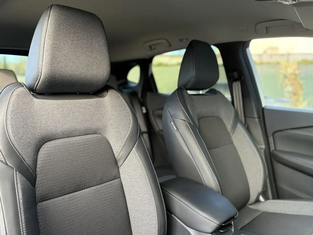 Vue intérieure rapprochée des sièges avant gris et noirs du Nissan Qashqai III e-Power 2025, avec accoudoir central.