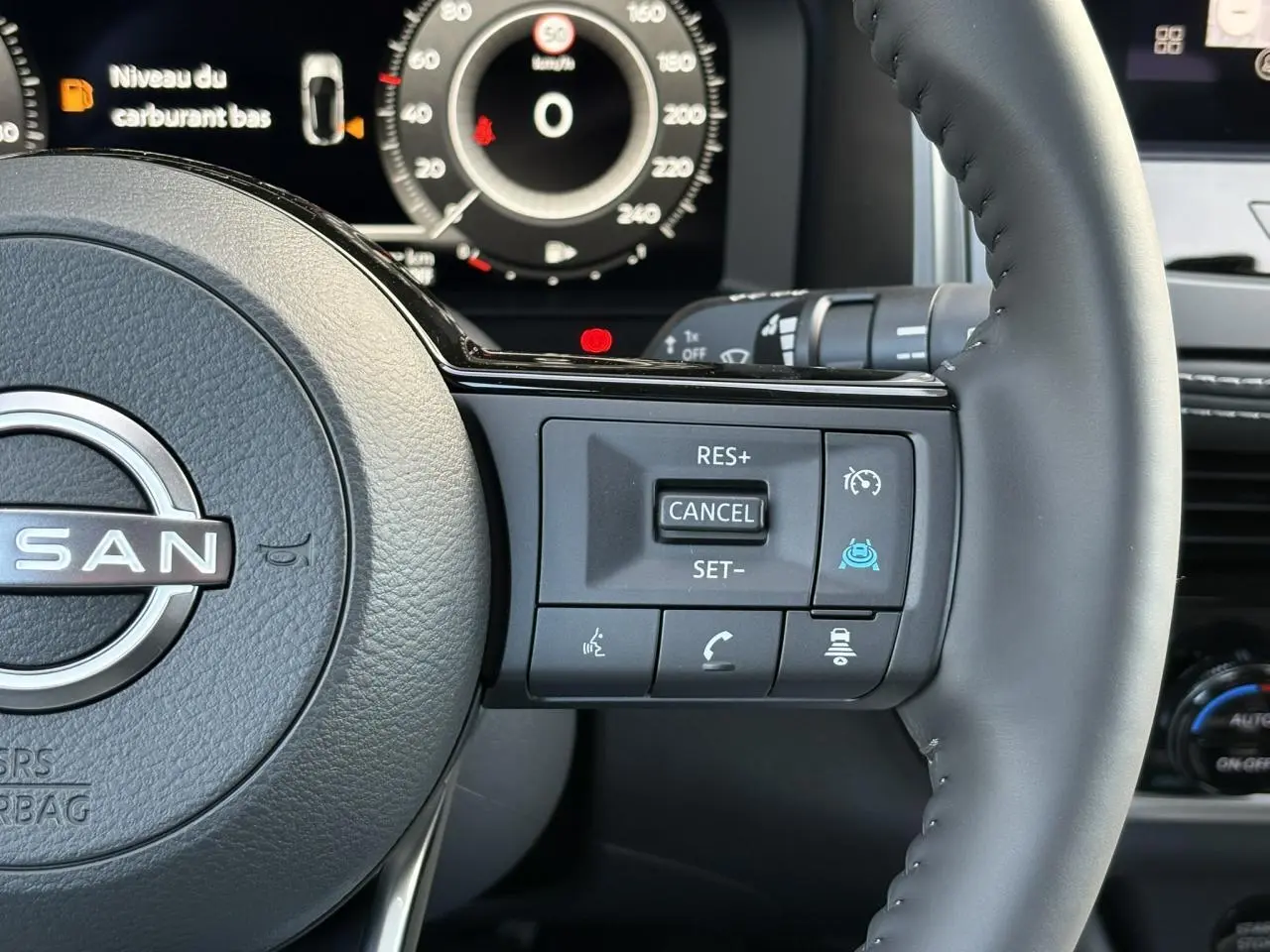 Gros plan sur le volant cuir du Nissan Qashqai blanc nacré, avec commandes de régulateur et affichage numérique en arrière-plan.