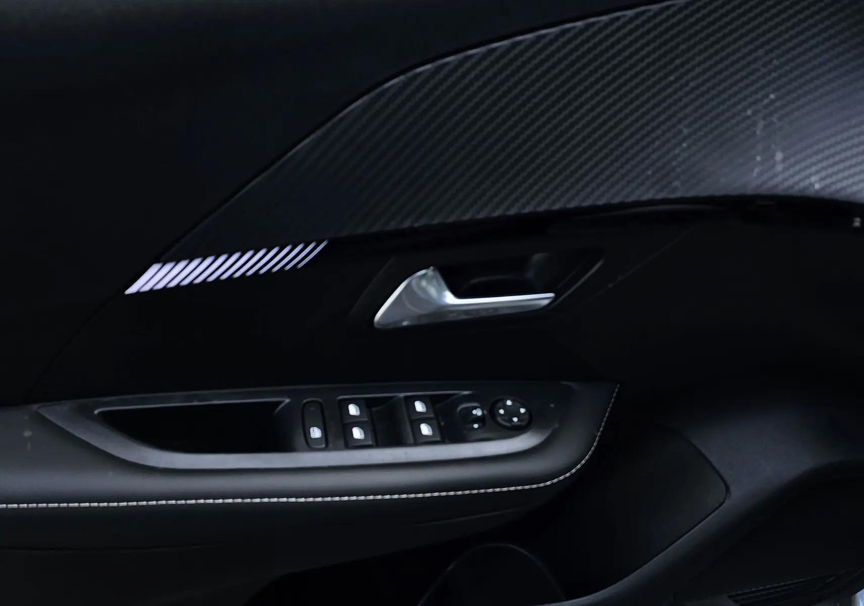 Détail de la porte intérieure côté conducteur de la Peugeot 208 grise, avec commandes des vitres et poignée argentée.
