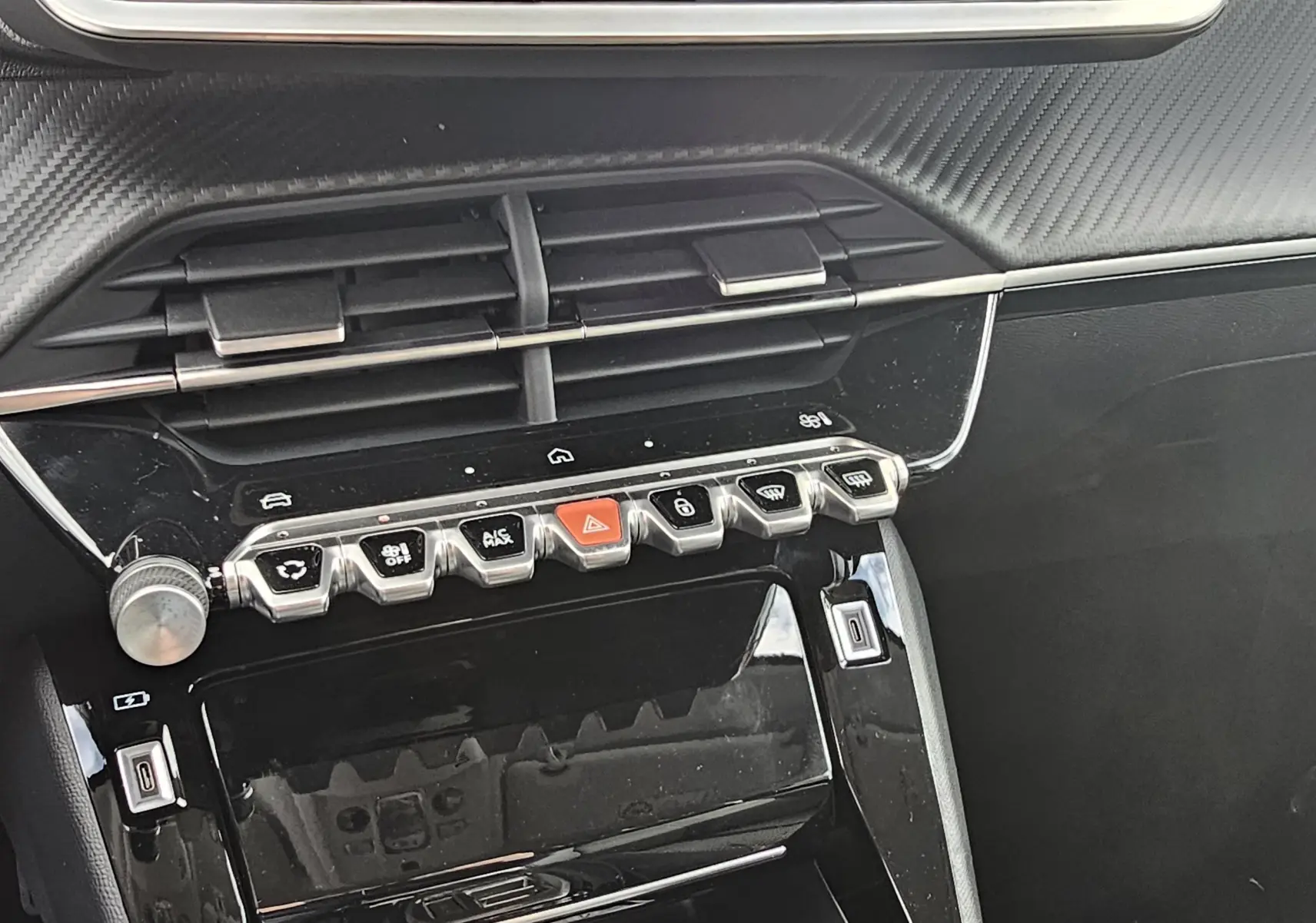 Détail de la console centrale noire brillante de la Peugeot 208 110 hybrid Allure avec boutons de commande et aérateurs.