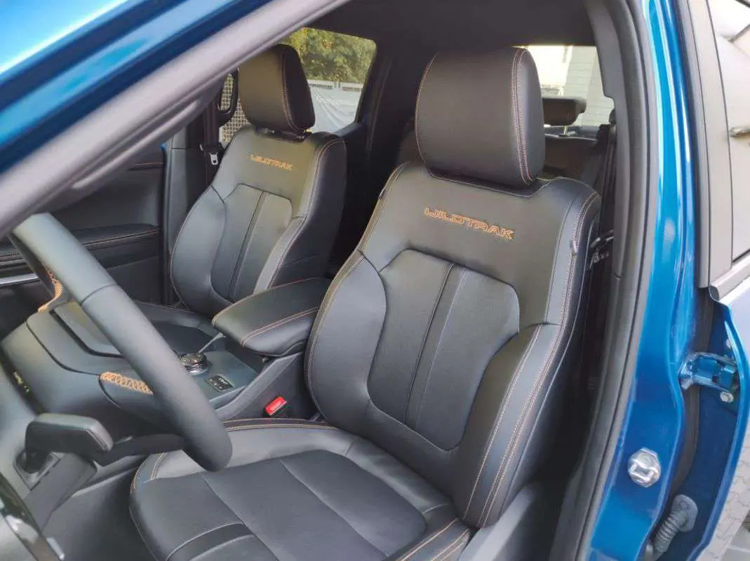 Vue intérieure côté conducteur du Ford Ranger Wildtrak 2025 bleu lightning, sièges cuir noirs avec surpiqûres orange et logo Wildtrak.