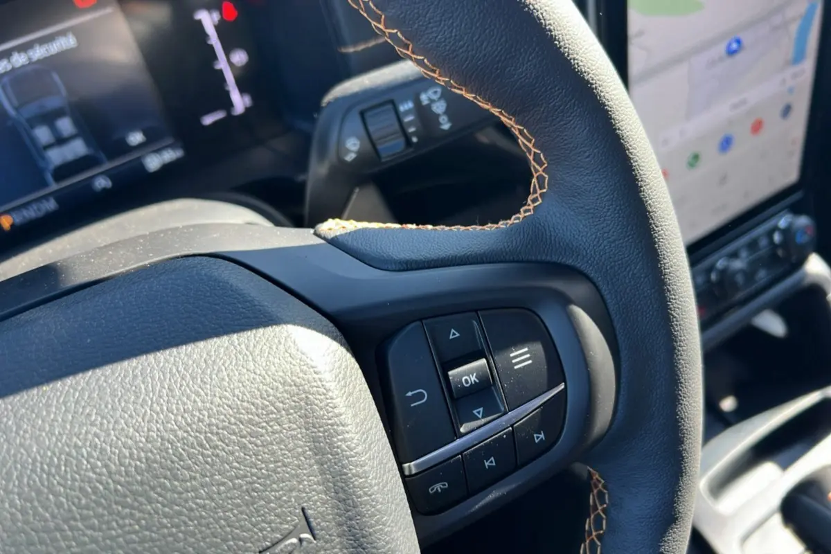 Gros plan sur le volant cuir noir avec surpiqûres marron du Ford Ranger Wildtrak 2025, tableau de bord et écran tactile en arrière-plan.