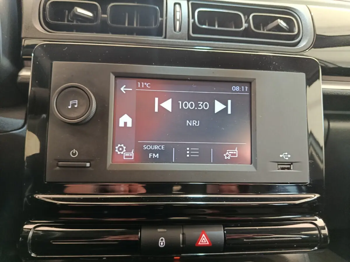Vue rapprochée de l’écran tactile multimédia noir de la Citroën C3 blanc, affichant la radio FM NRJ à 100.30 MHz.