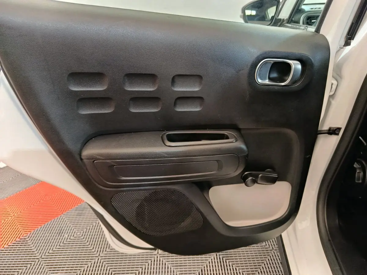 Vue rapprochée de la porte arrière droite noire avec poignée et commande de vitre manuelle d'une Citroën C3 blanche 2021.