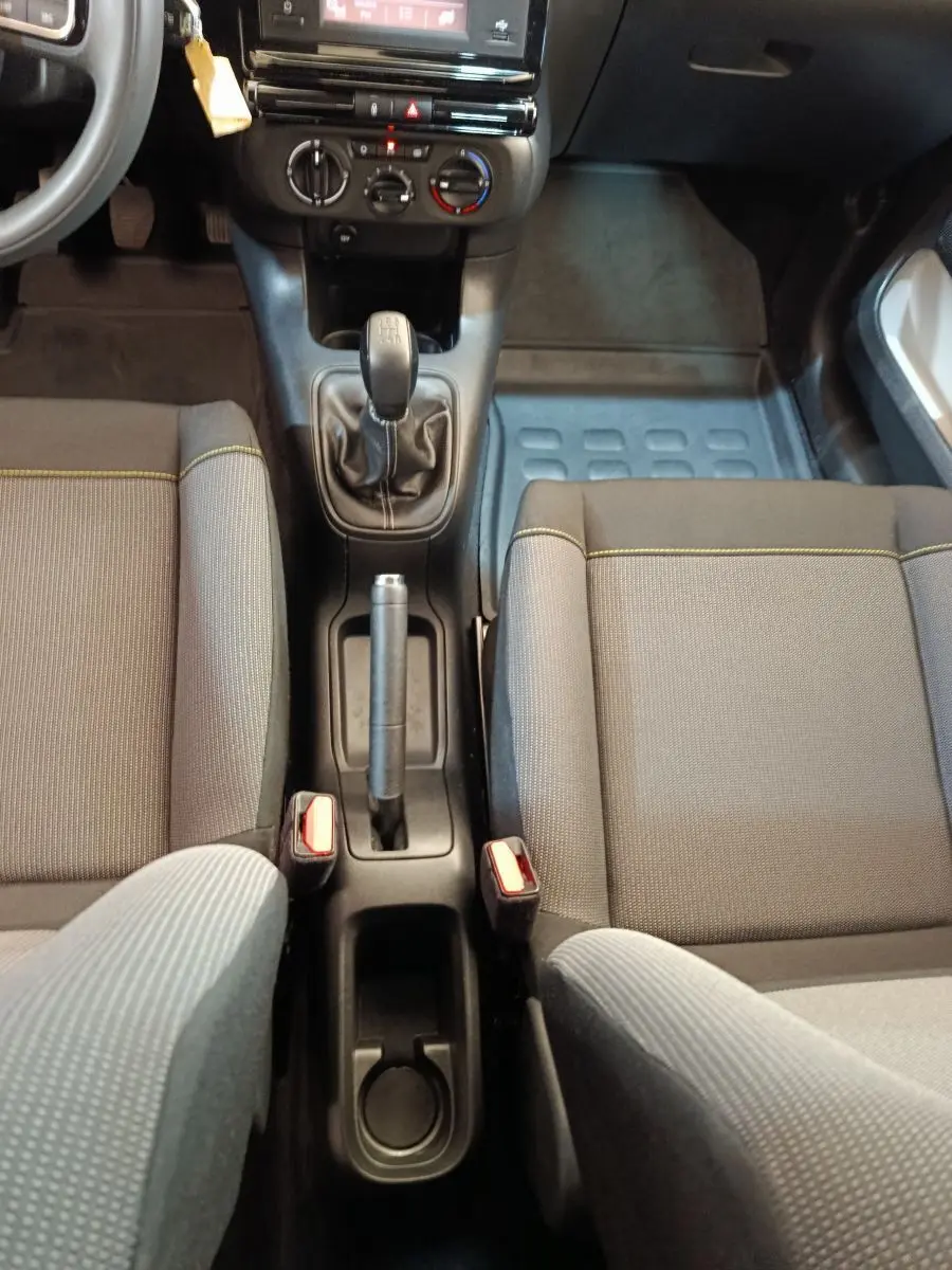 Vue intérieure centrée sur la console centrale et la boîte manuelle de la Citroën C3, sièges gris avec surpiqûres jaunes.
