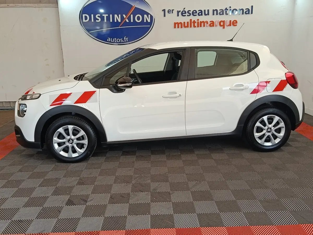 Vue de profil côté gauche d'une Citroën C3 blanche 2021 avec bandes rouges diagonales sur ailes avant et arrière.