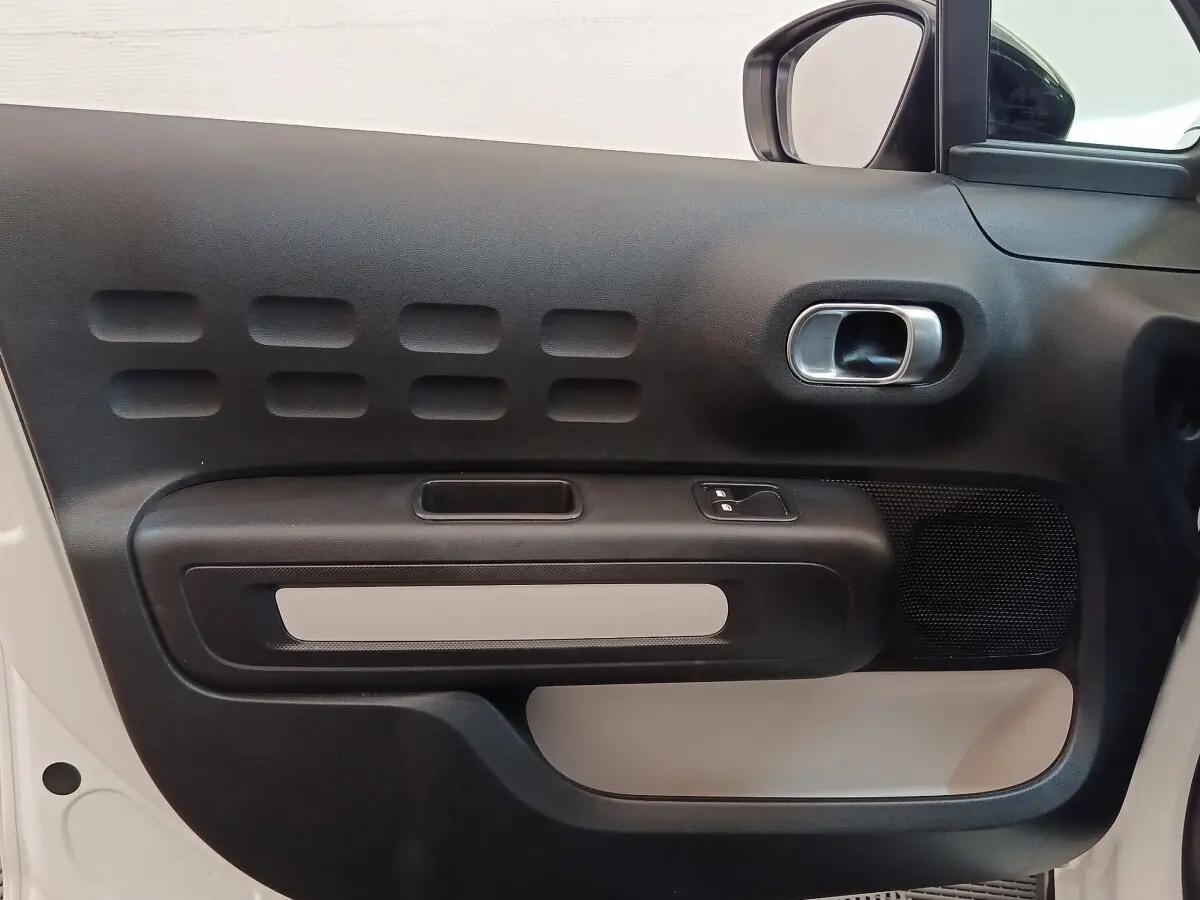 Gros plan sur la porte avant gauche noire et beige de la Citroën C3 blanche, mettant en valeur la poignée et les commandes.