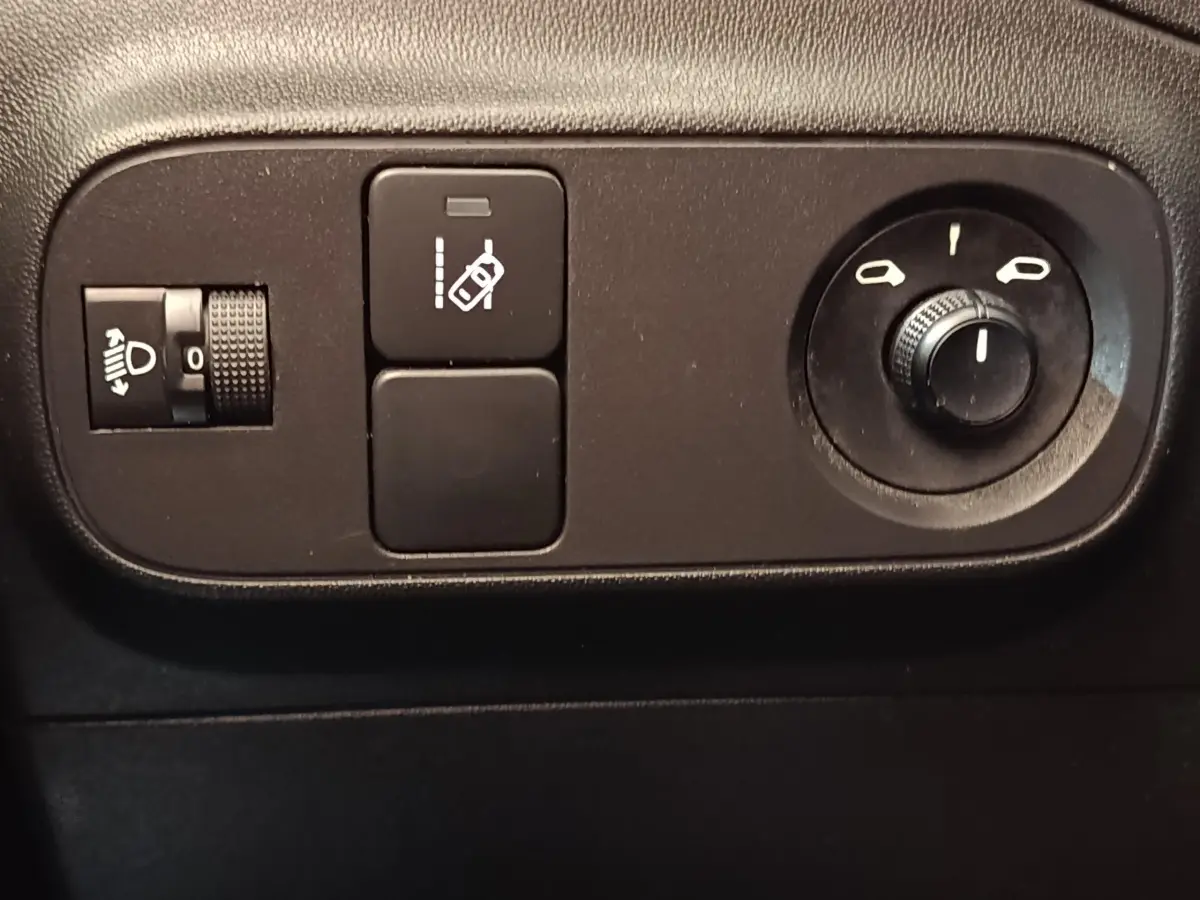 Gros plan sur les commandes intérieures noires du tableau de bord de la Citroën C3 blanche, avec réglage des phares et des rétroviseurs.
