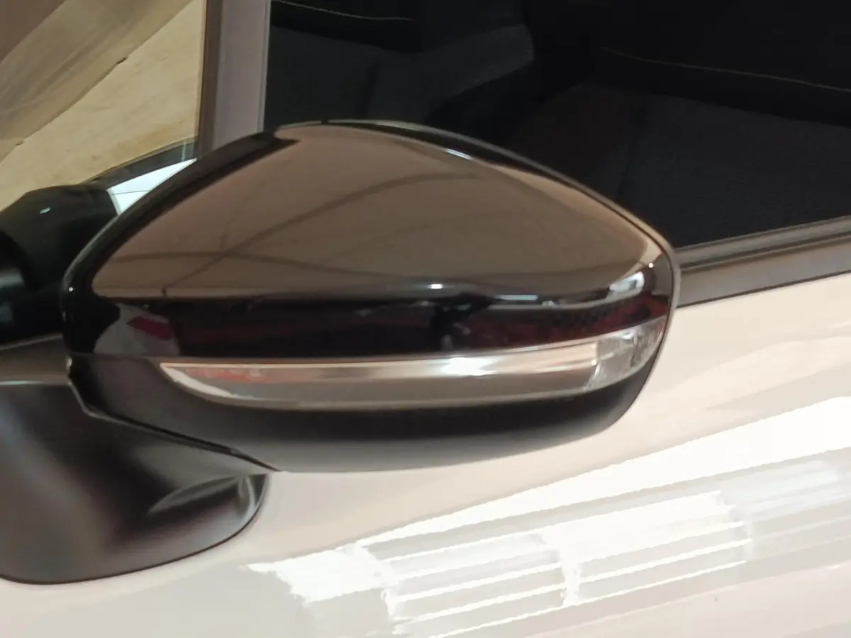 Gros plan sur le rétroviseur extérieur noir d'une Citroën C3 blanche, côté conducteur, avec clignotant intégré.