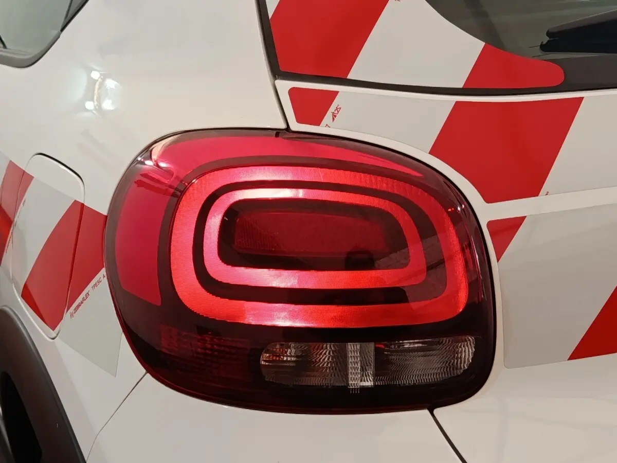 Gros plan sur le feu arrière droit rouge d'une Citroën C3 blanche avec motifs rouges géométriques.