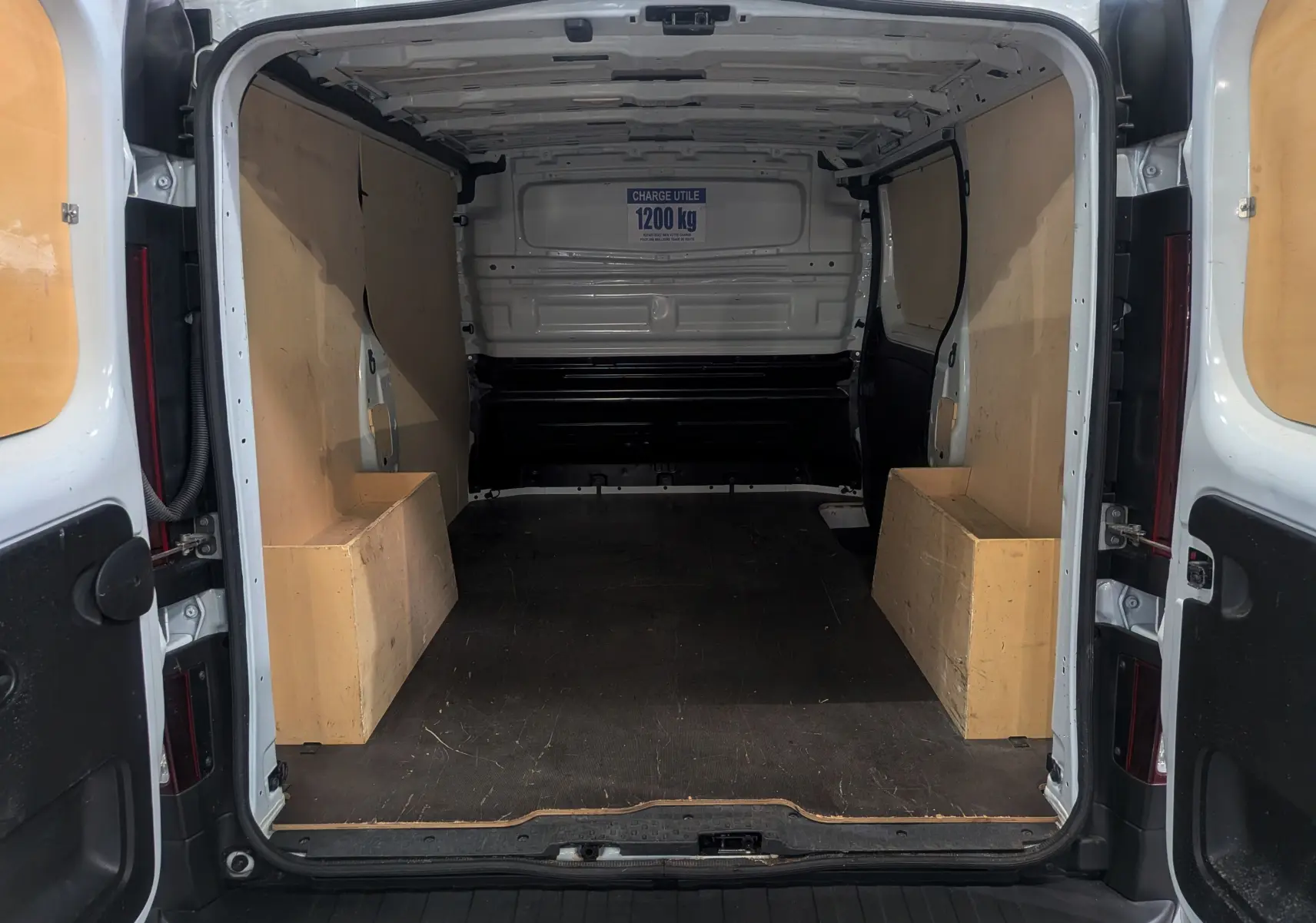 Vue arrière intérieure du Renault Trafic Fourgon blanc minéral 2024, montrant l'espace de chargement avec panneaux bois et capacité 1200 kg.