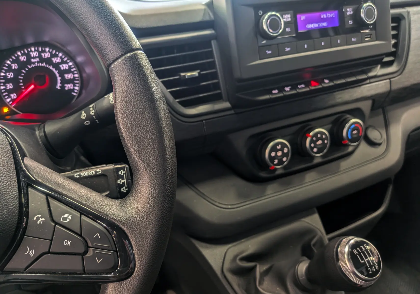 Vue intérieure centrée sur le volant et la console centrale du Renault Trafic Fourgon blanc, avec levier de vitesses manuel visible.